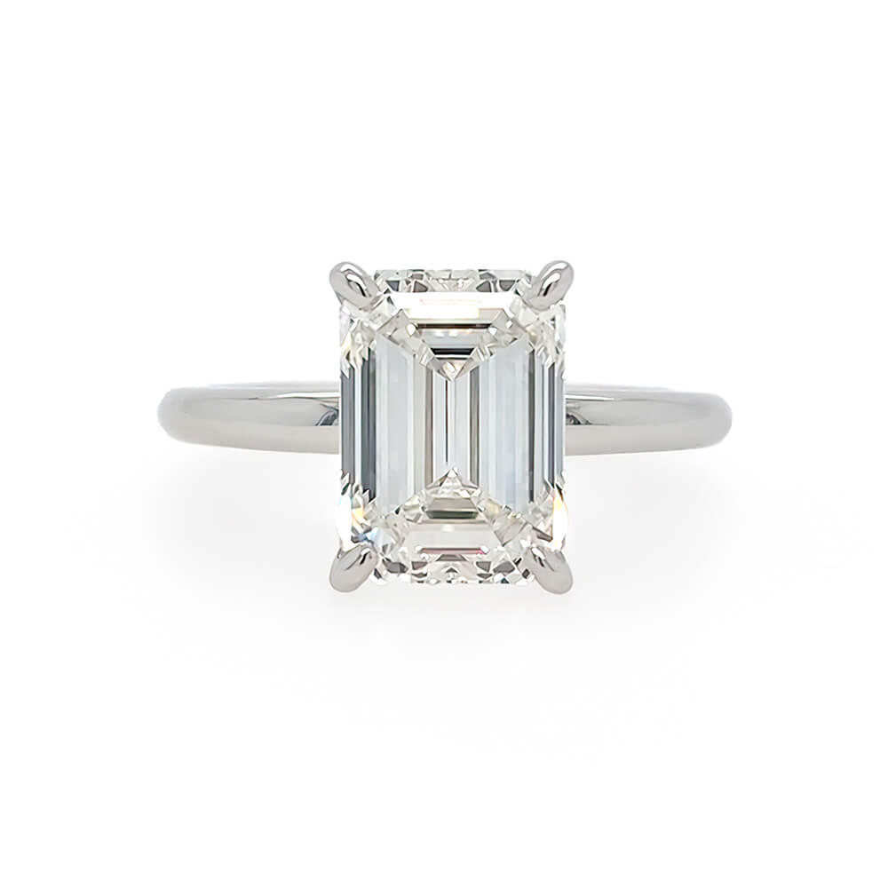 An emerald-cut diamond solitaire ring in a polished platinum metal band, set against a plain white background.