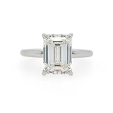 An emerald-cut diamond solitaire ring in a polished platinum metal band, set against a plain white background.