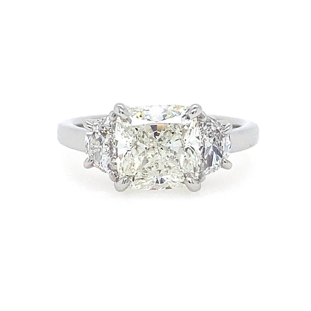 A three-stone diamond ring featuring a large rectangular cushion-cut center diamond flanked by two smaller half moon diamonds, set in a polished platinum metal band on a white background.