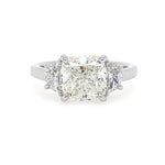 A three-stone diamond ring featuring a large rectangular cushion-cut center diamond flanked by two smaller half moon diamonds, set in a polished platinum metal band on a white background.