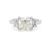 A three-stone diamond ring featuring a large rectangular cushion-cut center diamond flanked by two smaller half moon diamonds, set in a polished platinum metal band on a white background.