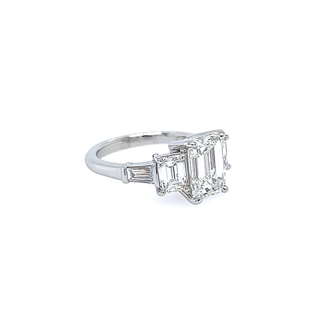 A custom platinum five-stone diamond ring featuring an emerald-cut center stone and baguette-cut side stones, set on a plain white background.