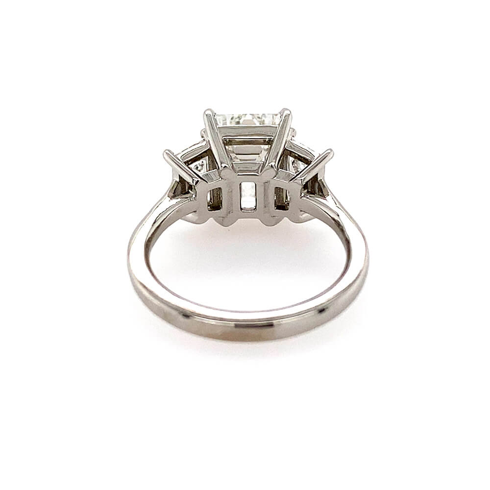 A platinum diamond ring with a three-stone cluster setting featuring an emerald cut center diamond and two trapezoid side stones, shown on a plain white background.