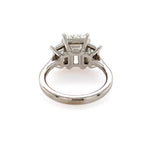 A platinum diamond ring with a three-stone cluster setting featuring an emerald cut center diamond and two trapezoid side stones, shown on a plain white background.