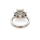 A platinum diamond ring with a three-stone cluster setting featuring an emerald cut center diamond and two trapezoid side stones, shown on a plain white background.