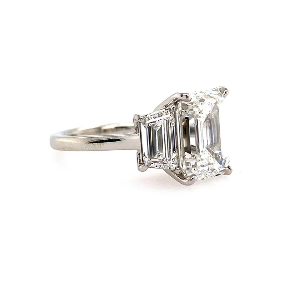 An emerald-cut diamond ring with a platinum band, shown on a plain white background.