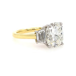An 18K yellow gold ring with a large cushion-cut diamond center stone and two trapezoid diamonds on either side, set in a platinum metal, shown on a plain white background.