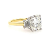 An 18K yellow gold ring with a large cushion-cut diamond center stone and two trapezoid diamonds on either side, set in a platinum metal, shown on a plain white background.