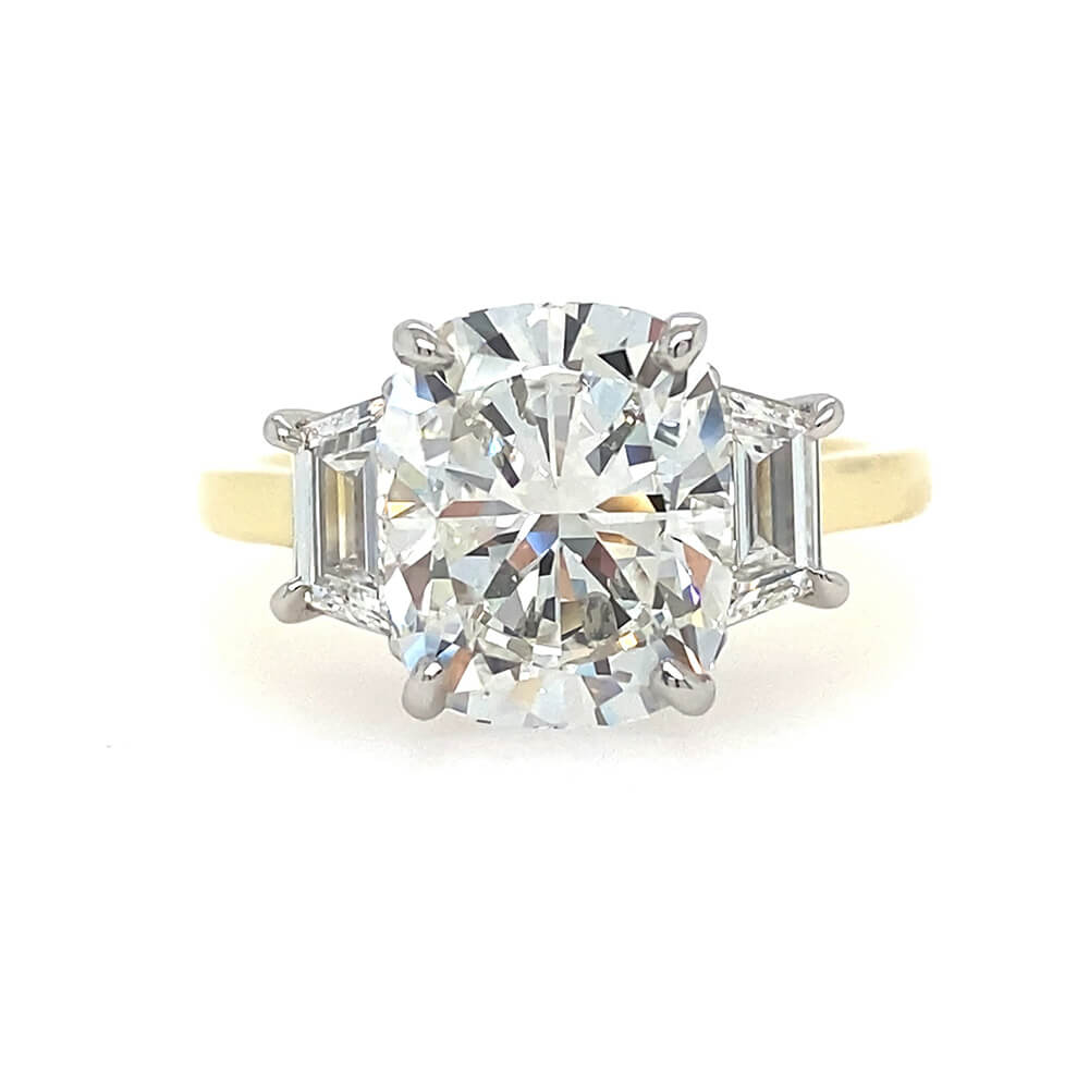 A three-stone diamond ring featuring a large elongated cushion cut center diamond flanked by two trapezoid side diamonds on an 18K yellow gold band, set against a plain white background.