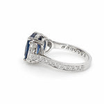 A platinum ring featuring a cushion-cut blue sapphire center stone and smaller clear half moon diamonds on the shoulders, set against a plain white background.