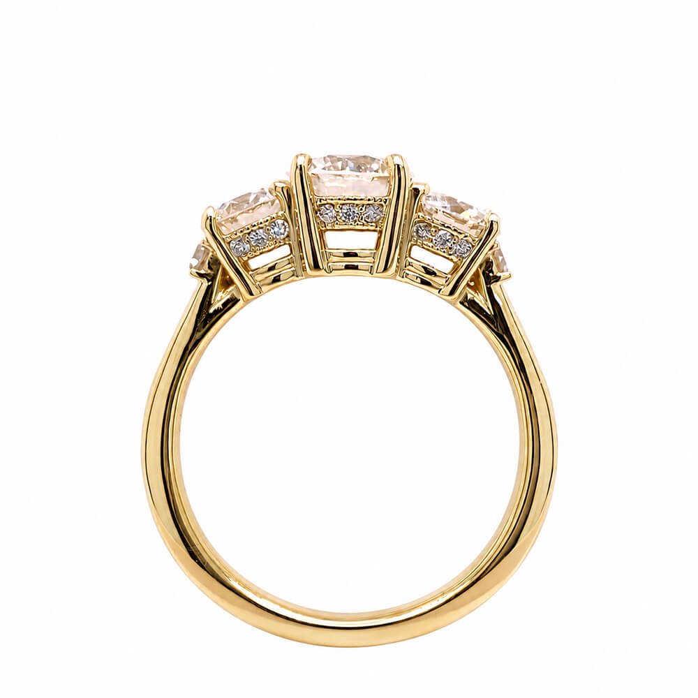 An 18K yellow gold three-stone ring with large center diamond and smaller diamonds on either side, shown on a plain white background.
