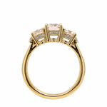 An 18K yellow gold three-stone ring with large center diamond and smaller diamonds on either side, shown on a plain white background.