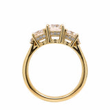 An 18K yellow gold three-stone ring with large center diamond and smaller diamonds on either side, shown on a plain white background.