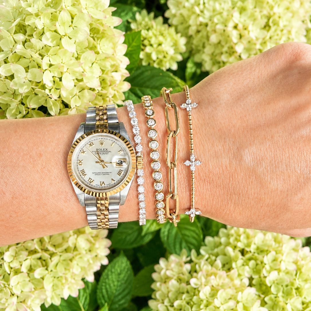 woman wearing a rolex watch with four bracelets including a diamond tennis bracelet, a yellow gold bezel set diamond tennis bracelet, a gold link bracelet and a yellow gold bangle with diamond accents