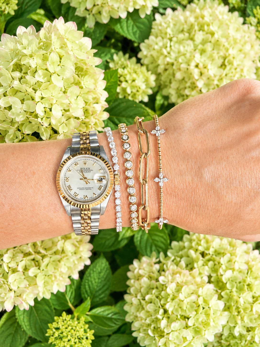 woman wearing a rolex watch with four bracelets including a diamond tennis bracelet, a yellow gold bezel set diamond tennis bracelet, a gold link bracelet and a yellow gold bangle with diamond accents