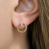A close-up of a woman's ear wearing a gold hoop earring with three small clear diamonds stacked vertically on the post.
