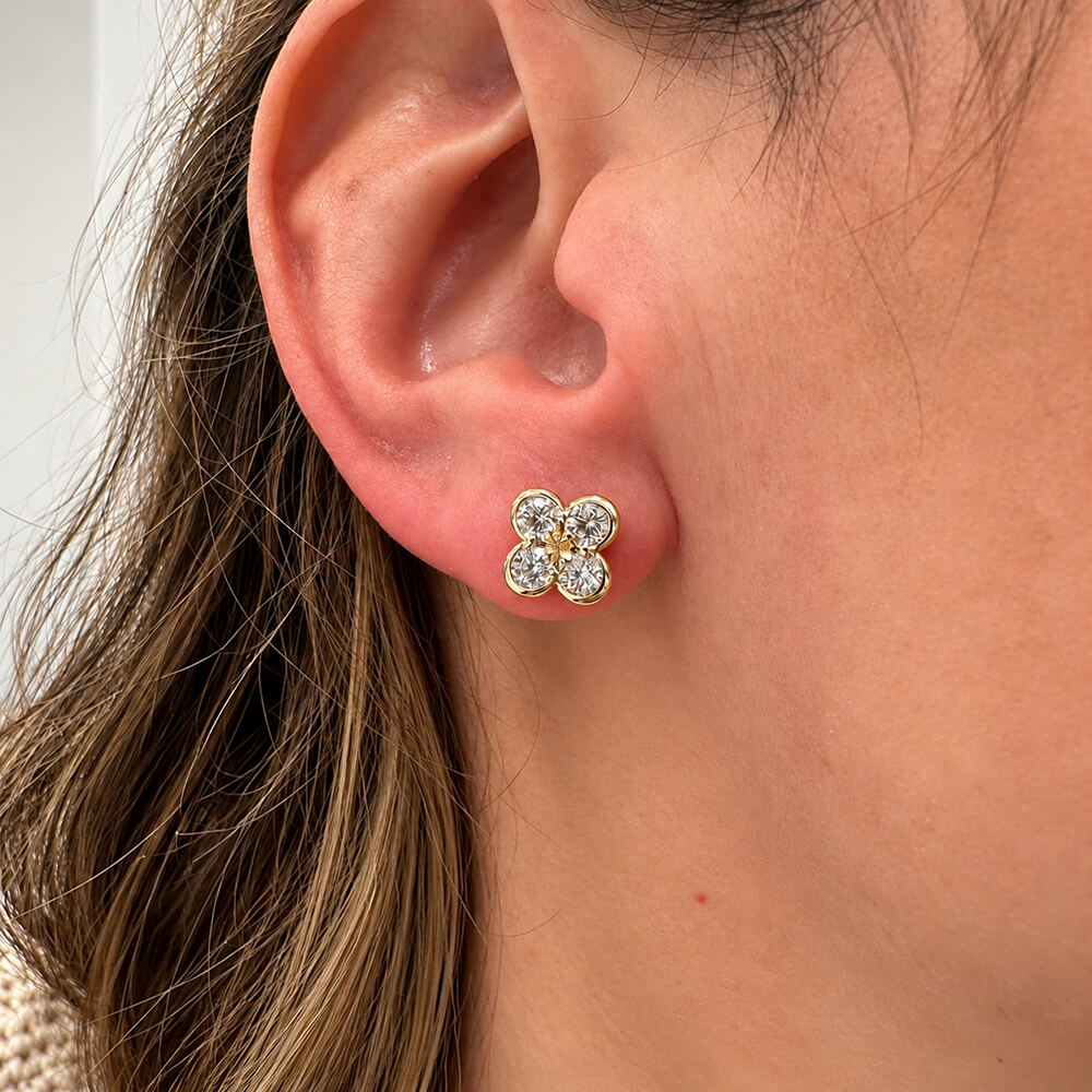 Close-up of a woman's ear wearing a clover shaped earring with diamonds in 14k yellow gold. 