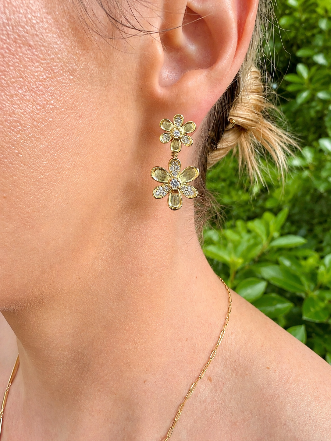 woman wearing yellow gold and pave diamond flower shaped drop earrings featuring two flowers on each one