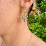 woman wearing yellow gold and pave diamond flower shaped drop earrings featuring two flowers on each one