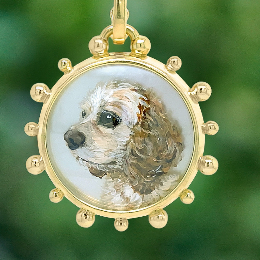 A round gold pendant necklace featuring a hand-painted portrait of a brown and white dog on a white background, set in a gold bezel with decorative ball accents around the edge.