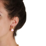 Close-up of a woman wearing a gold earring with a pink gemstone on a white background