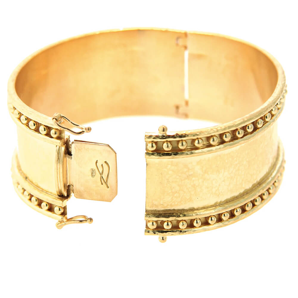 A wide 19k yellow gold cuff bracelet with a textured hand hammered finish, beaded borders on both edges, and a sliding clasp closure, shown on a plain white background.