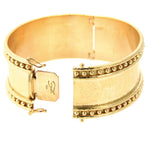 A wide 19k yellow gold cuff bracelet with a textured hand hammered finish, beaded borders on both edges, and a sliding clasp closure, shown on a plain white background.