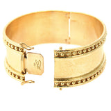 A wide 19k yellow gold cuff bracelet with a textured hand hammered finish, beaded borders on both edges, and a sliding clasp closure, shown on a plain white background.