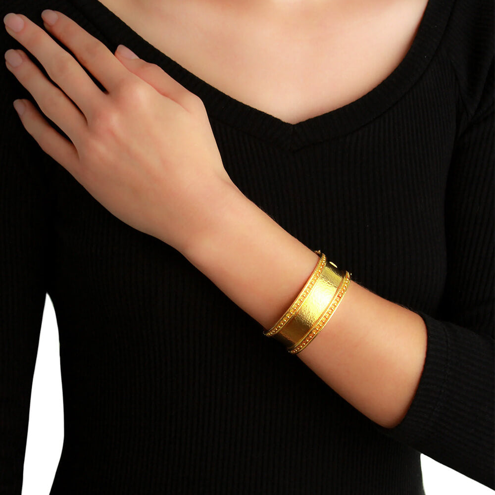 A close-up of a woman wearing a wide, polished Elizabeth Locke 19k yellow gold bangle bracelet on their wrist, paired with a black ribbed long-sleeve top.