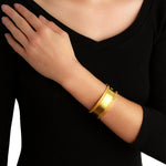 A close-up of a woman wearing a wide, polished Elizabeth Locke 19k yellow gold bangle bracelet on their wrist, paired with a black ribbed long-sleeve top.