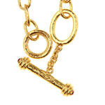 Elizabeth Locke 19k yellow gold link bracelet with a toggle clasp featuring textured oval links, a short chain connector, and a cylindrical toggle bar with small red ruby gemstone accents at the ends, shown on a white background.