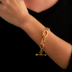A 19k yellow gold chain bracelet with oval links and a toggle clasp designed by Elizabeth Locke, worn on a person's wrist against a black top.