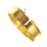 A wide, hammered 19k yellow gold bangle bracelet with a sliding clasp closure designed by Elizabeth Locke, shown on a plain white background.