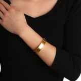 A close-up of a woman wearing a polished 19k yellow gold bangle bracelet designed by Elizabeth Locke, wearing a black ribbed long-sleeve top.