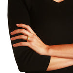 A close-up of a woman's hand wearing a delicate gold ring with green aquamarine gemstones, styled with a black ribbed knit top against a white background.