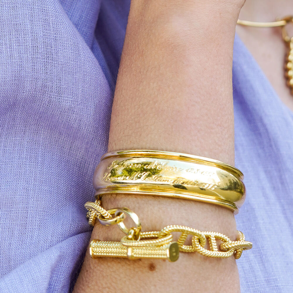 18K Gold bracelets on a wrist with a purple fabric background