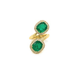 A ring with two emerald stones surrounded by smaller diamonds set in a gold band