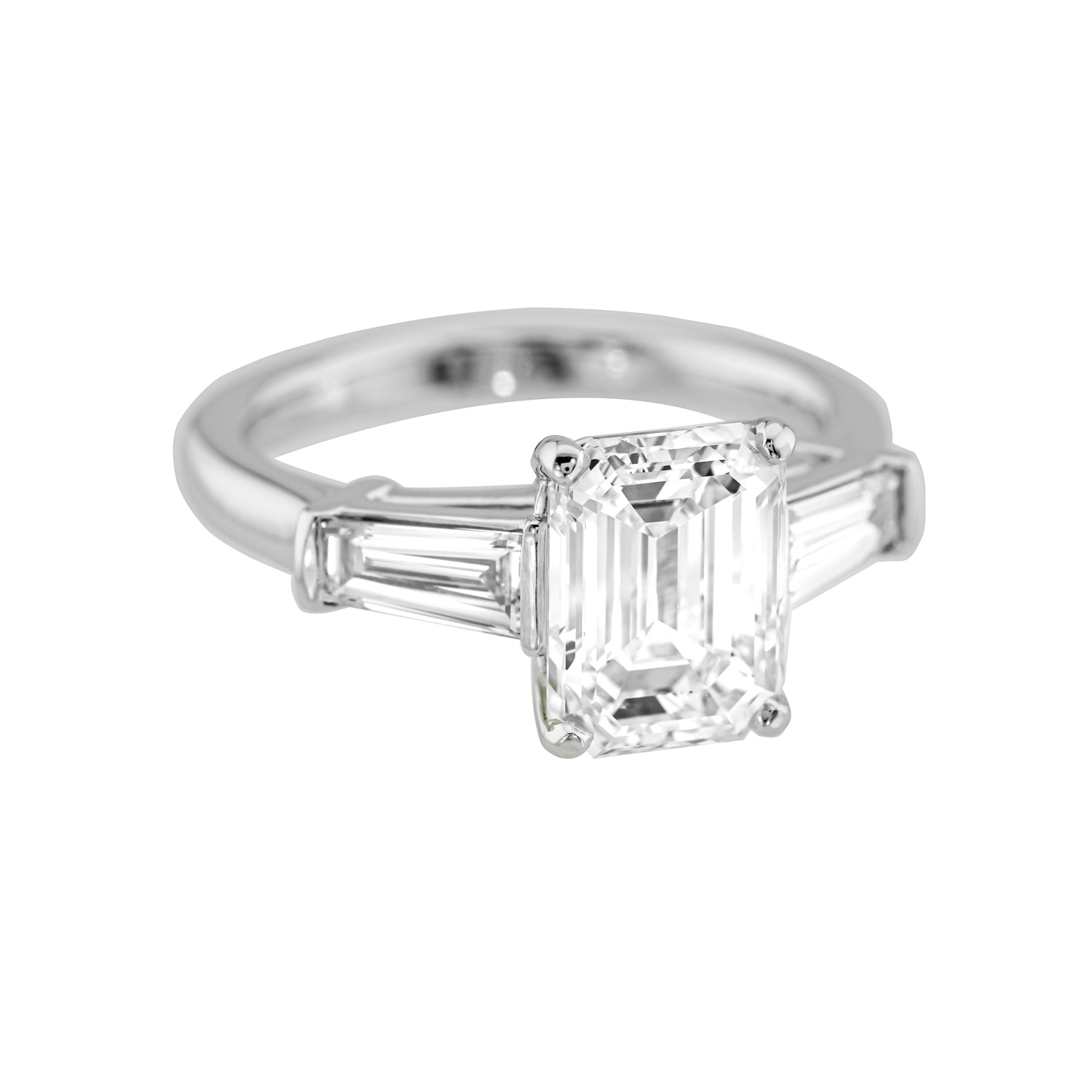A platinum emerald cut diamond ring with tapered baguettes, featuring a clear and well-cut emerald in the center, flanked by two smaller diamonds