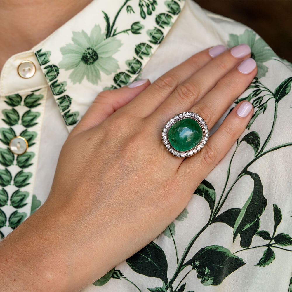 Woman's hand wearing a large emerald gemstone ring with diamonds