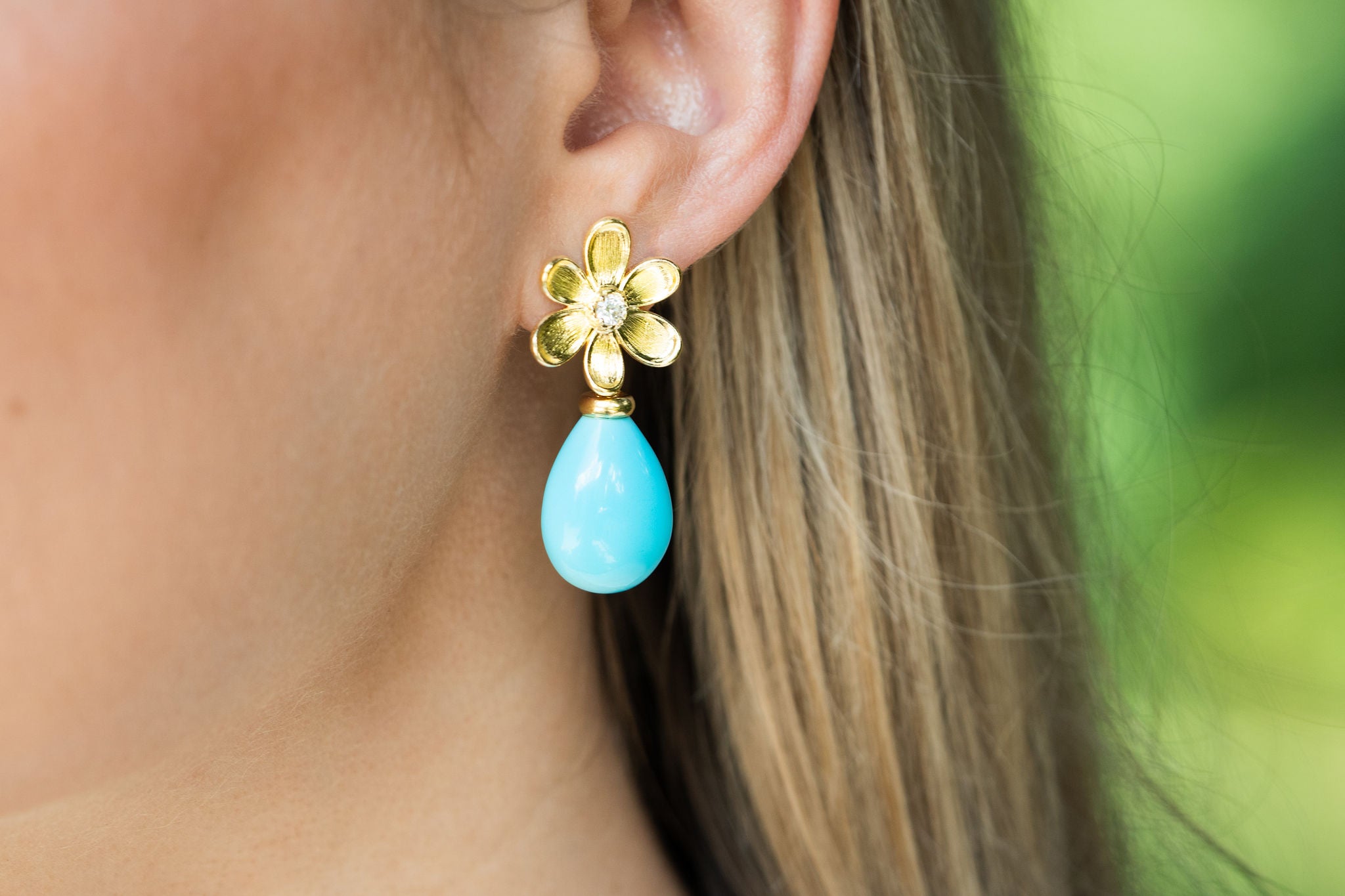 Close-up of a woman wearing an 18K gold earring with a blue turquoise teardrop pendant.