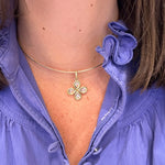 Close-up of a woman wearing a gold necklace with a clover-shaped white sapphire pendant, against a blurred purple shirt background.