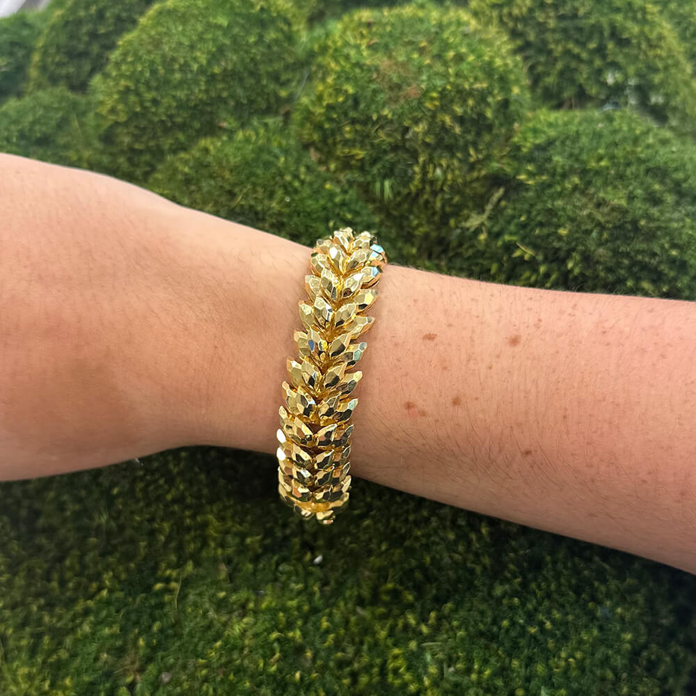Henry Dunay 18k yellow gold bracelet on a woman's wrist against a green moss background