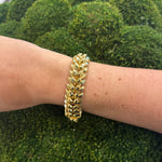 Henry Dunay 18k yellow gold bracelet on a woman's wrist against a green moss background