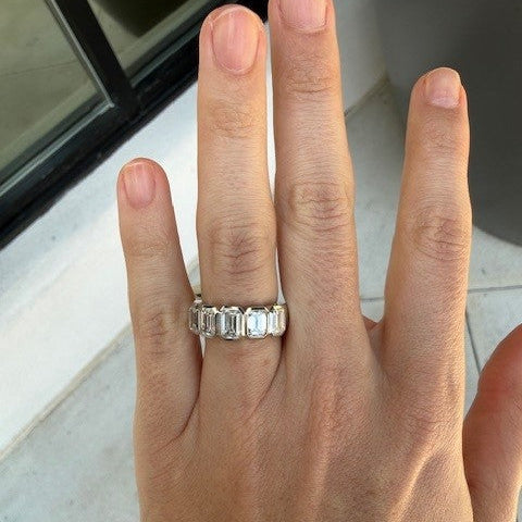 Woman's hand wearing a platinum ring with diamonds on a neutral background