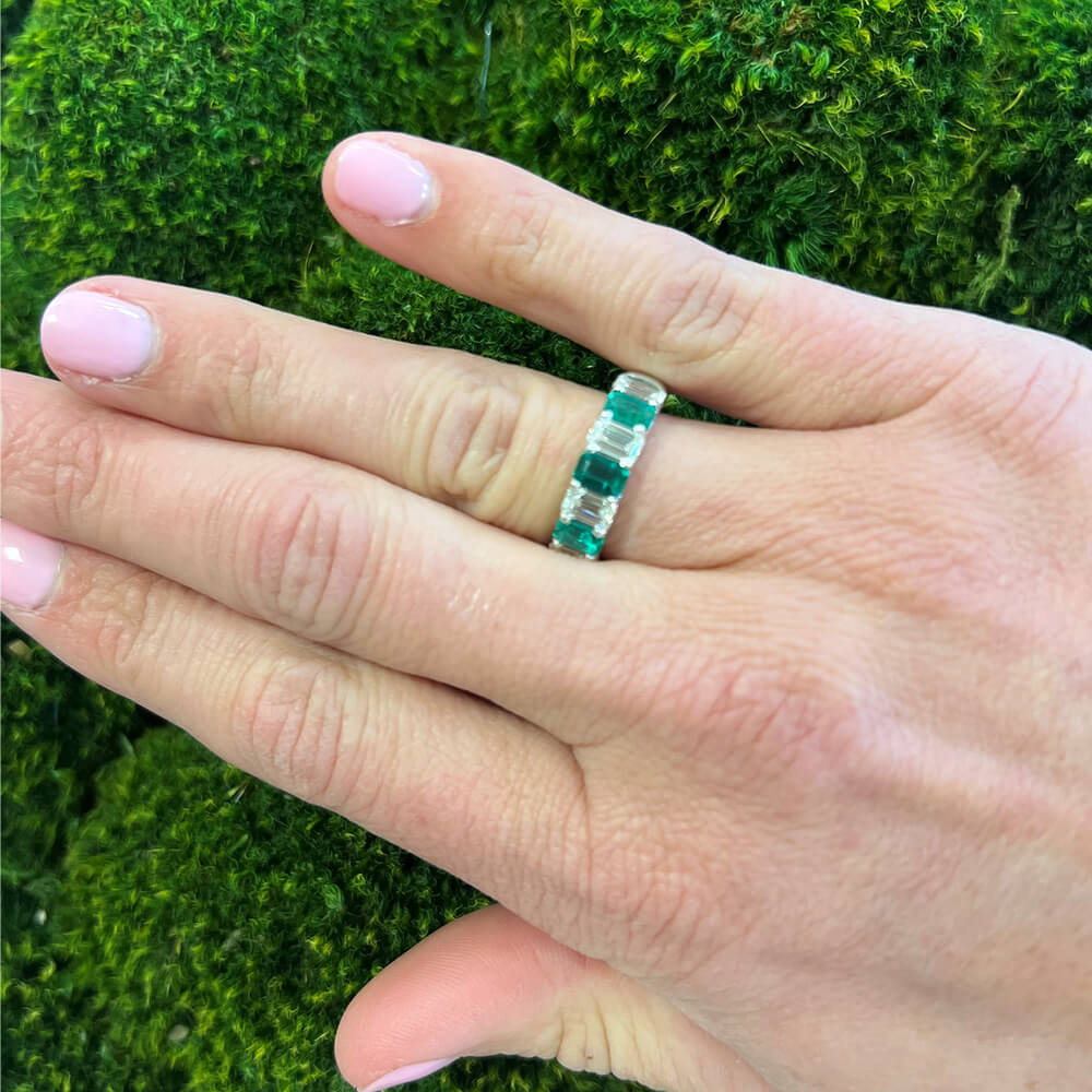 woman's hand wearing a green emerald ring and diamond band ring