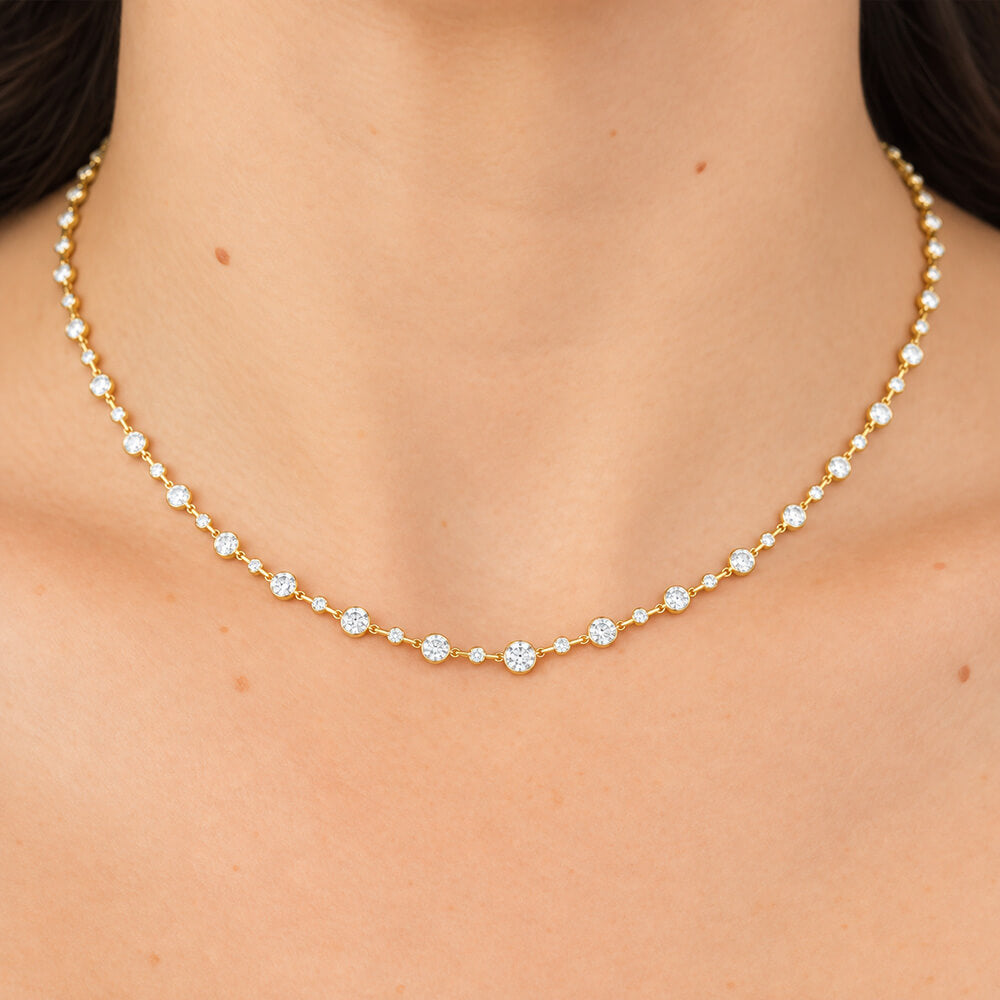 A delicate 18K yellow gold necklace with small clear diamonds worn on a model's neck, shown in a close-up shot.