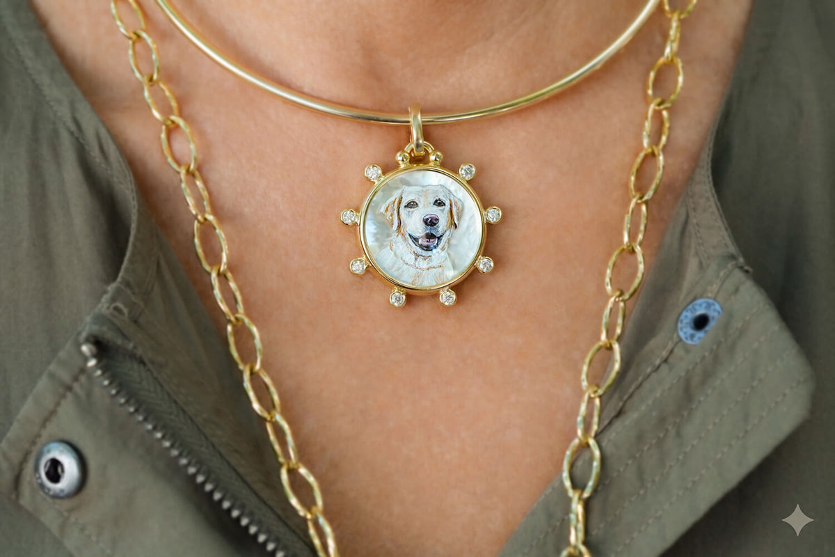 A close-up of a person wearing layered necklaces, including a gold chain necklace with a circular pendant featuring a custom pet portrait of a golden retriever on a white background with small rhinestone accents.