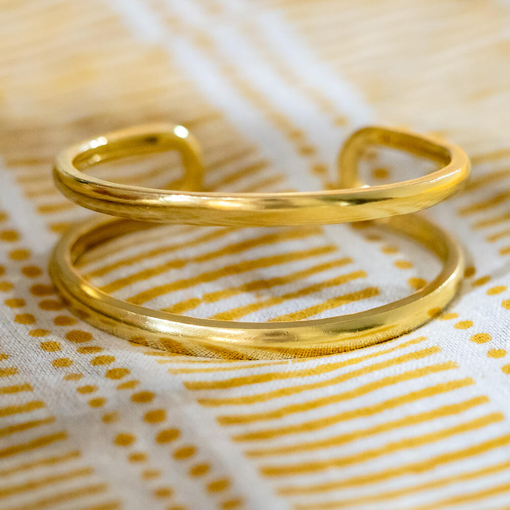 A polished 18k yellow gold open cuff bracelet resting on a white fabric napkin with yellow stripes and dots
