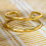 A polished 18k yellow gold open cuff bracelet resting on a white fabric napkin with yellow stripes and dots