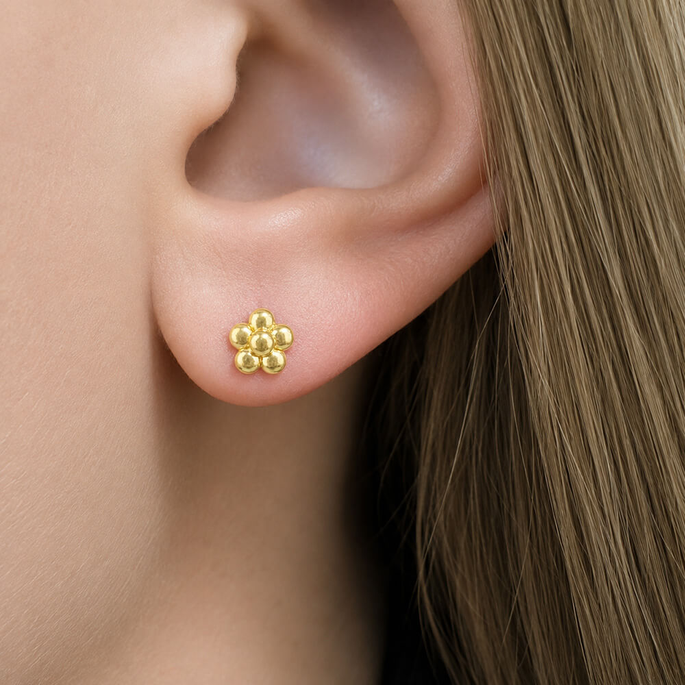 A close-up of a woman's ear wearing an 18K yellow gold flower stud earring designed by Laura Pearce.